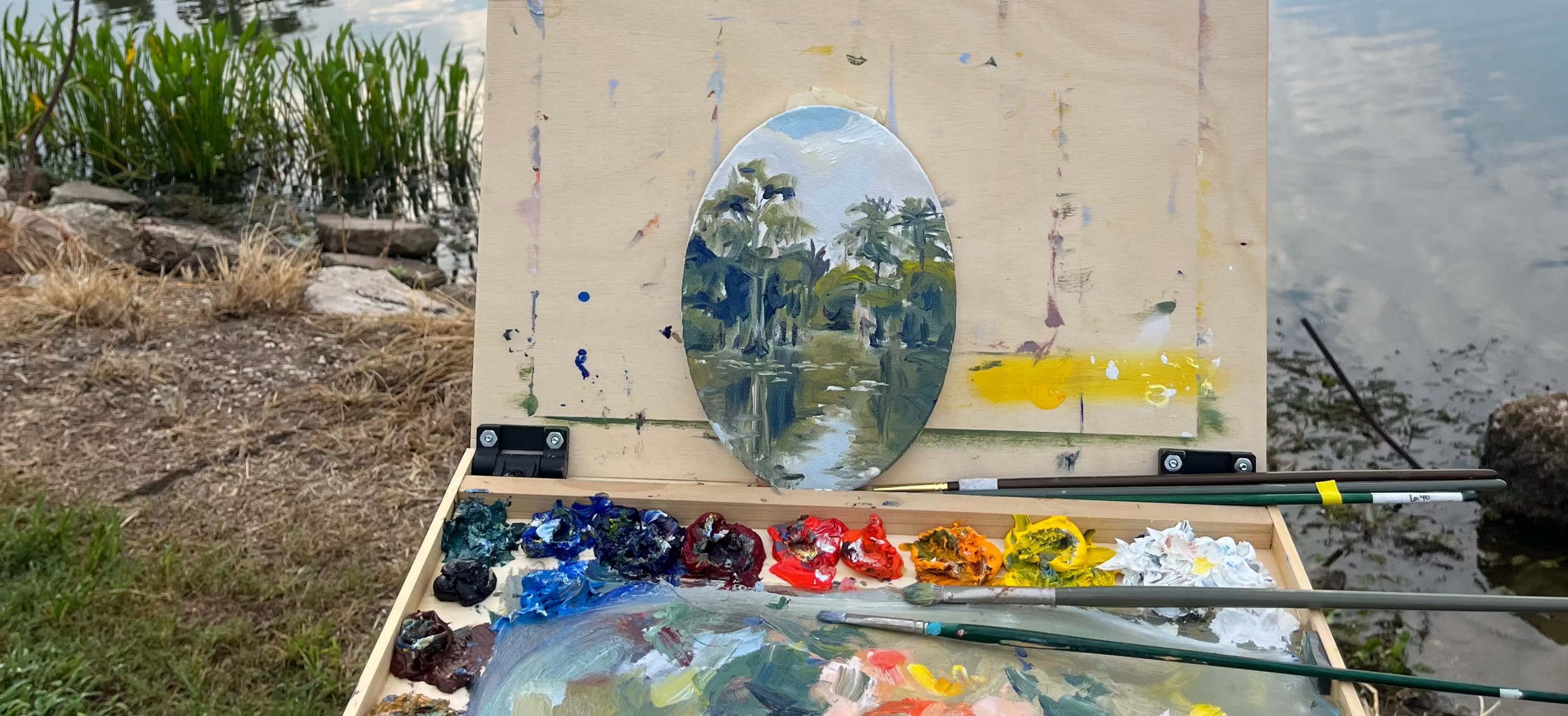 Painting set up outdoors by a lake with a scenic background